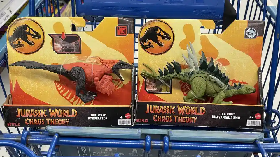 Two 'Jurassic World Chaos Theory' dinosaur toys, a red and black Pyroraptor and a green Huayangosaurus, sit side-by-side in…