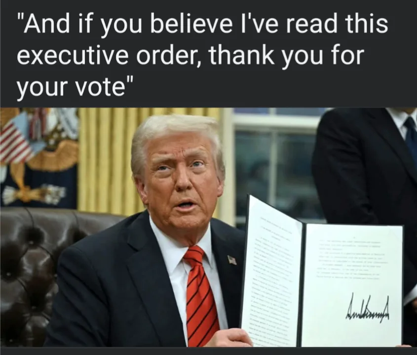 A man in a dark suit and red striped tie sits in an office holding an open document with a signature at the bottom. Behind…