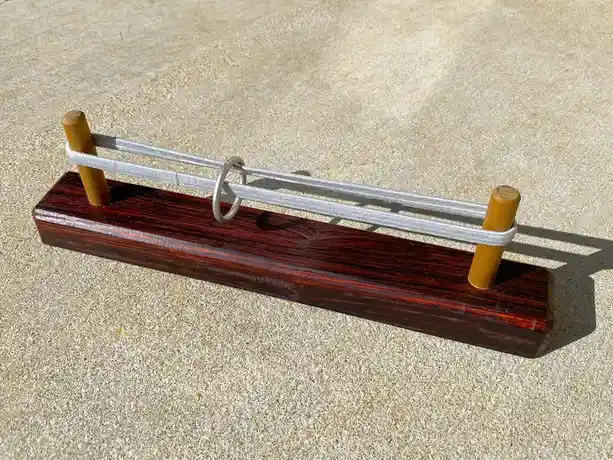 A wooden puzzle toy with two vertical dowels and a silver ring threaded through a white elastic band, resting on a polished…
