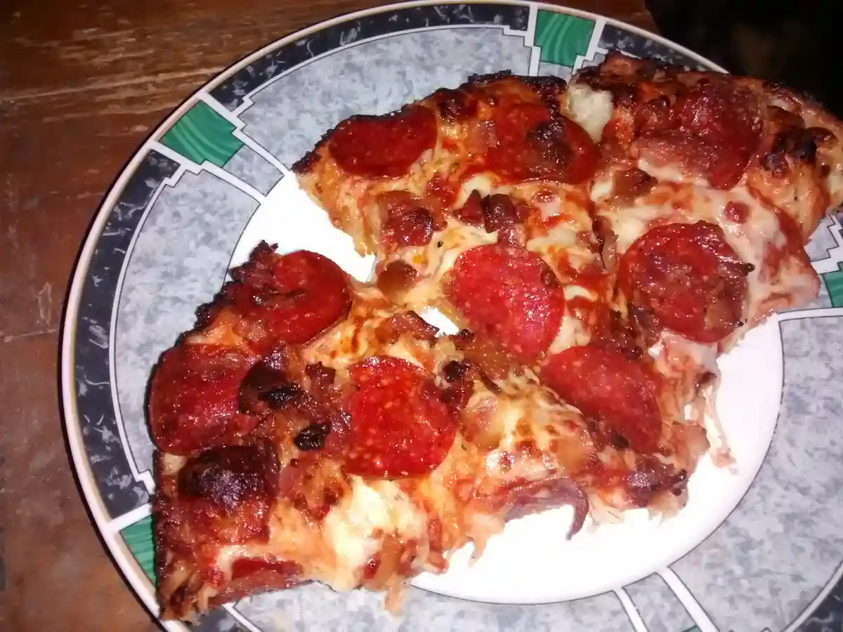 A close-up photo shows several slices of pepperoni pizza on a decorative plate with a gray, black, and green geometric…