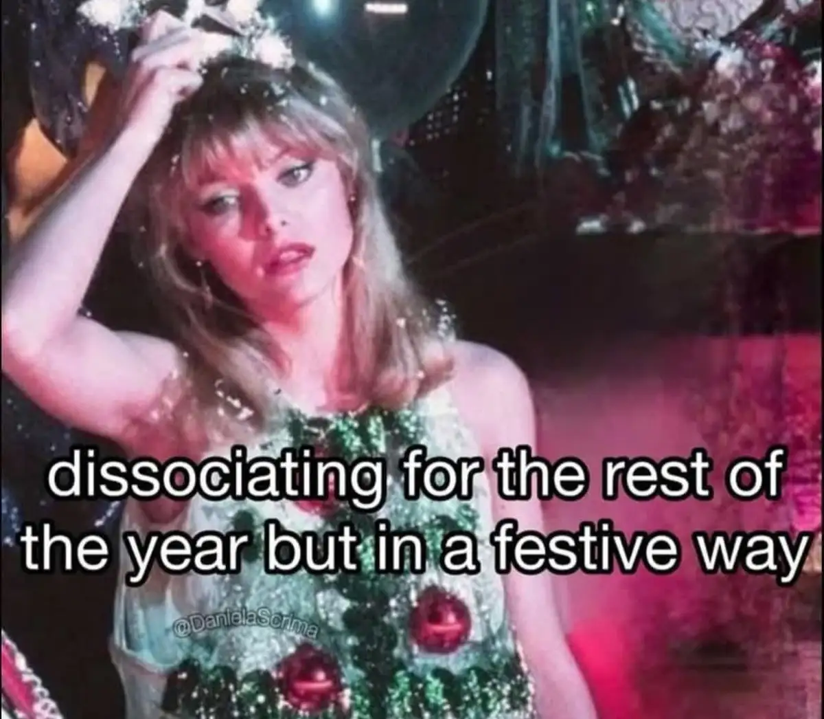 A woman in a sparkly green dress decorated with red ornaments, resembling a christmas tree, looks tired while holding…