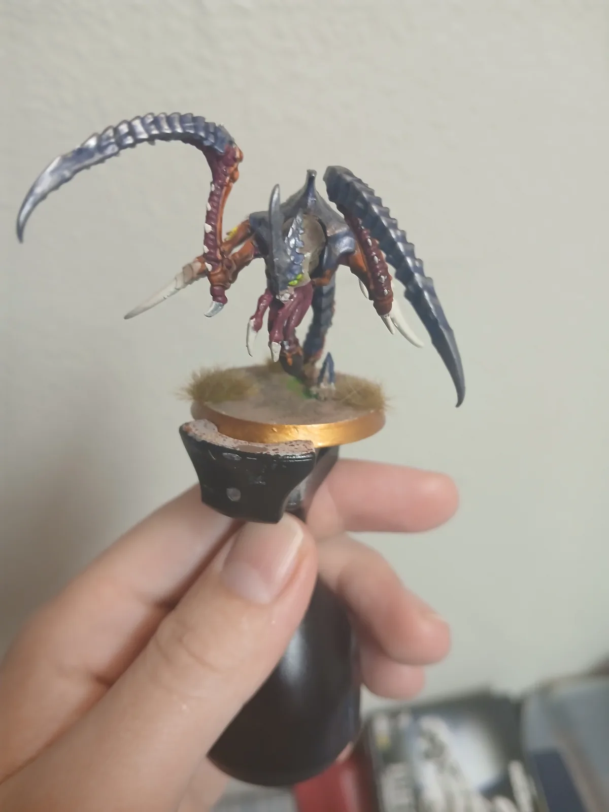 A hand holds a painted miniature of a fantasy creature with large, curved, dark blue horns, sharp claws, and a menacing…