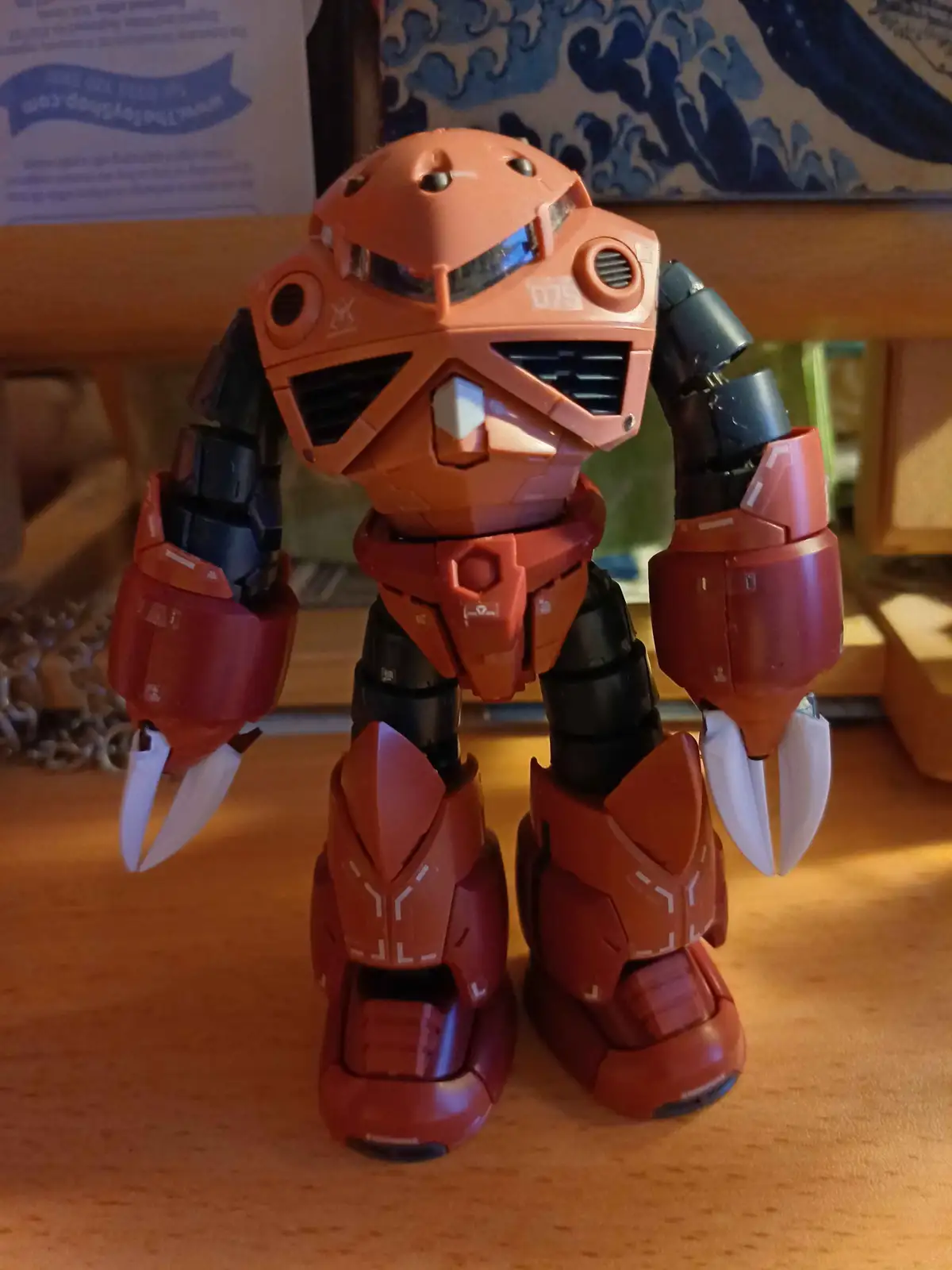 A small orange and black robot toy with white claw-like hands stands on a wooden surface. The robot has a blocky, angular…