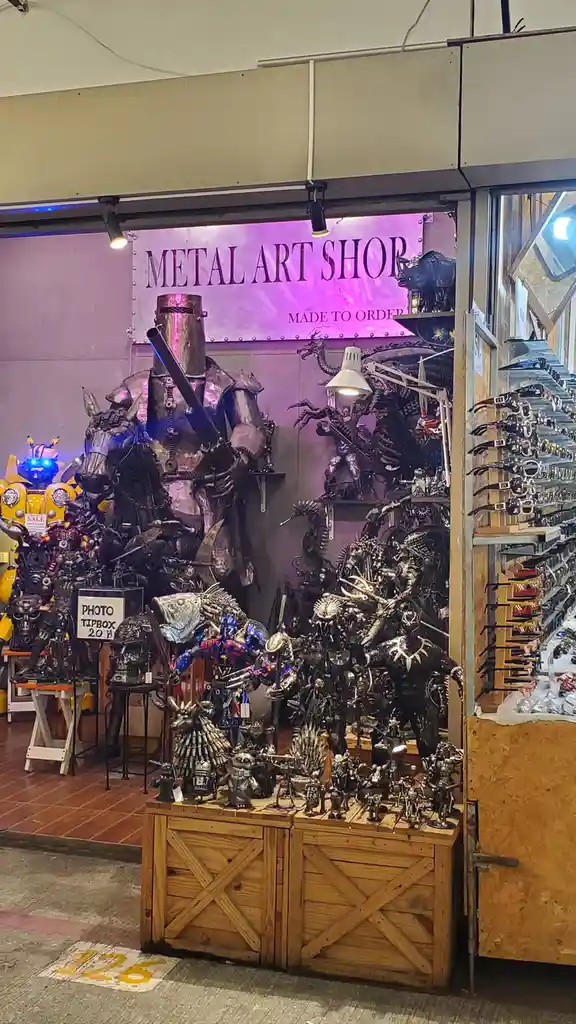 A storefront labeled 'METAL ART SHOP' displays an extensive collection of intricate metal sculptures, including a large…
