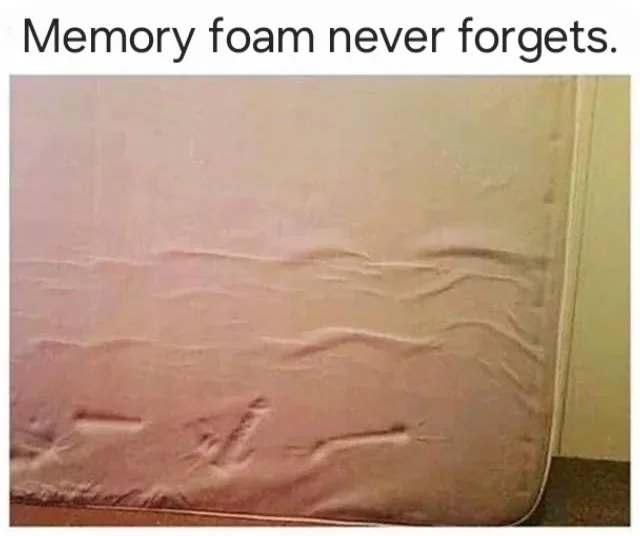 A close-up photo of a light-colored memory foam mattress showing deep, permanent indentations from previous use. The…