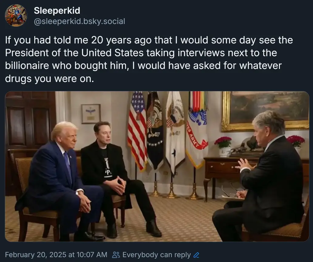 Three men are seated in an official-looking room with American flags and military banners in the background. Two men sit…