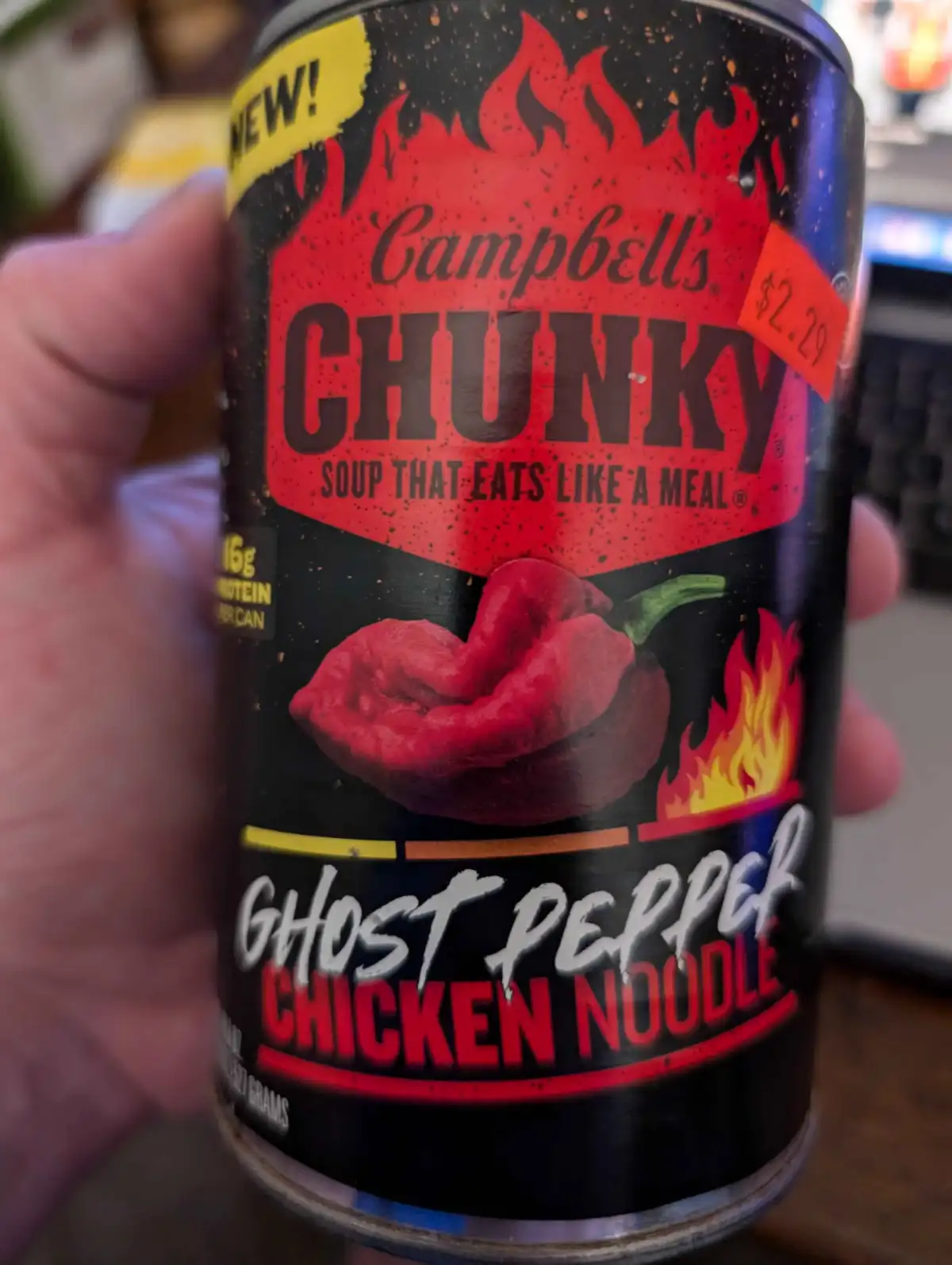 A hand holds a Campbell's Chunky soup can labeled 'Ghost Pepper Chicken Noodle,' featuring a large red ghost pepper and…