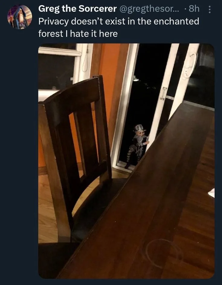 A photo shows a small figurine of a fantasy character peeking through a doorway into a room with a wooden table and chair…