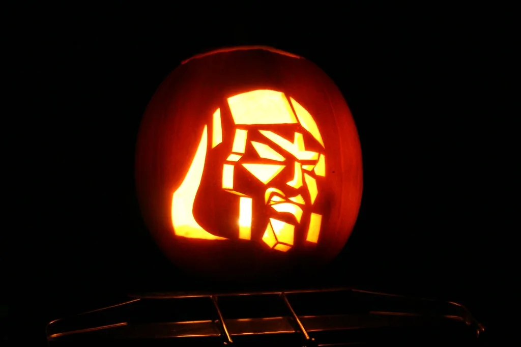 A carved pumpkin with a glowing orange interior, illuminated from within, displays a stylized, angular face resembling a…