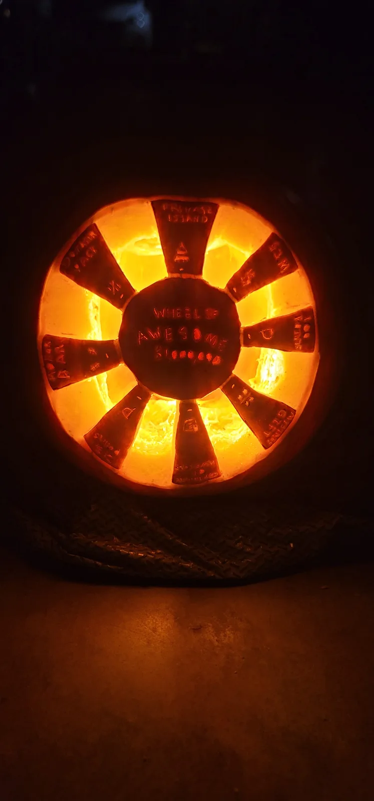 A carved pumpkin illuminated from within, shaped like a wheel with eight spokes. The center reads 'WHEEL OF AWESOME…