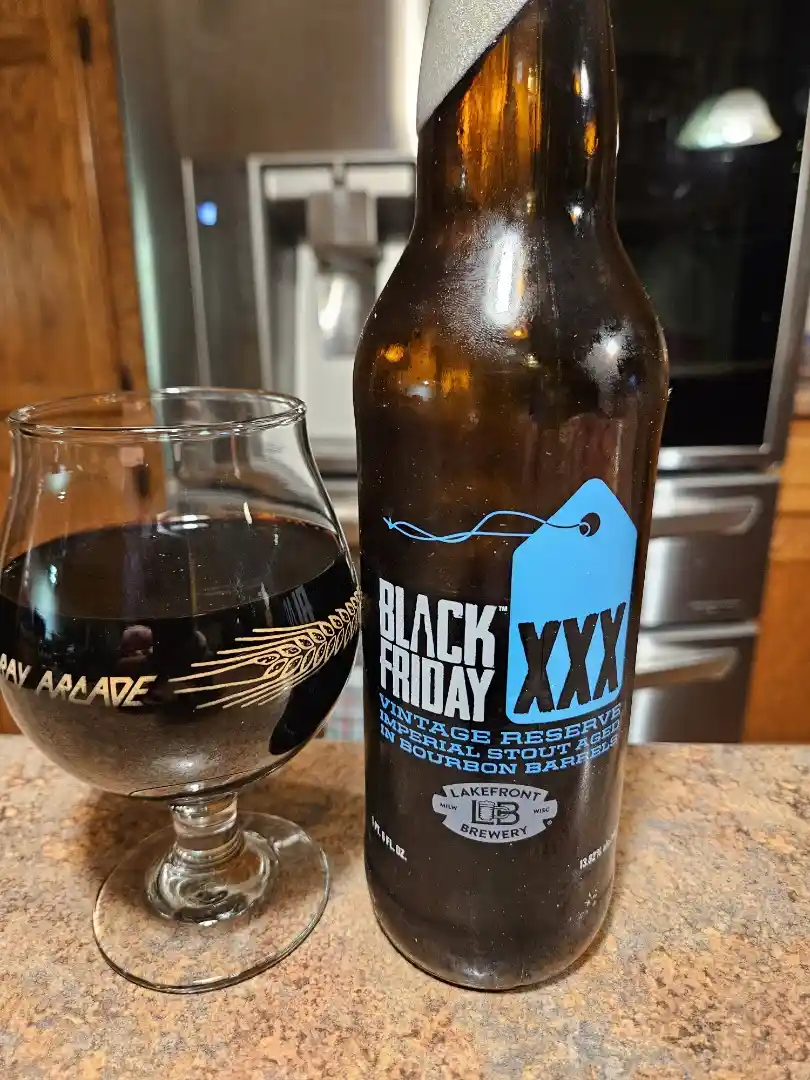A brown beer bottle labeled 'BLACK FRIDAY XXX VINTAGE RESERVE IMPERIAL STOUT AGED IN BOURBON BARRELS' sits next to a glass…
