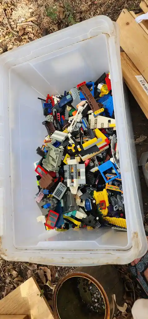 A white plastic storage bin is filled to the brim with a chaotic pile of colorful Lego bricks and pieces of various shapes…
