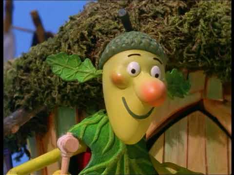 A cheerful, anthropomorphic yellow acorn character wearing a mossy cap and leafy clothing stands in front of a moss-covered…
