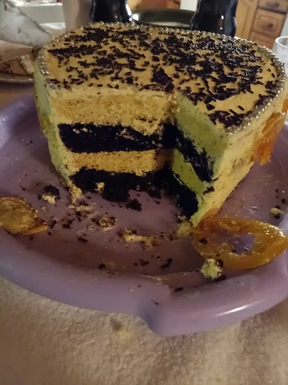A partially eaten layered cake with alternating light yellow and dark chocolate cake layers, topped with chocolate sprinkles…