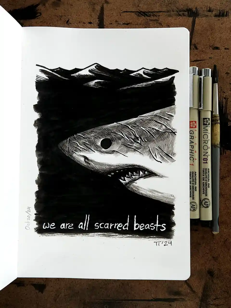 A black-and-white ink drawing in a sketchbook depicts a menacing shark emerging from dark water, its mouth open and teeth…