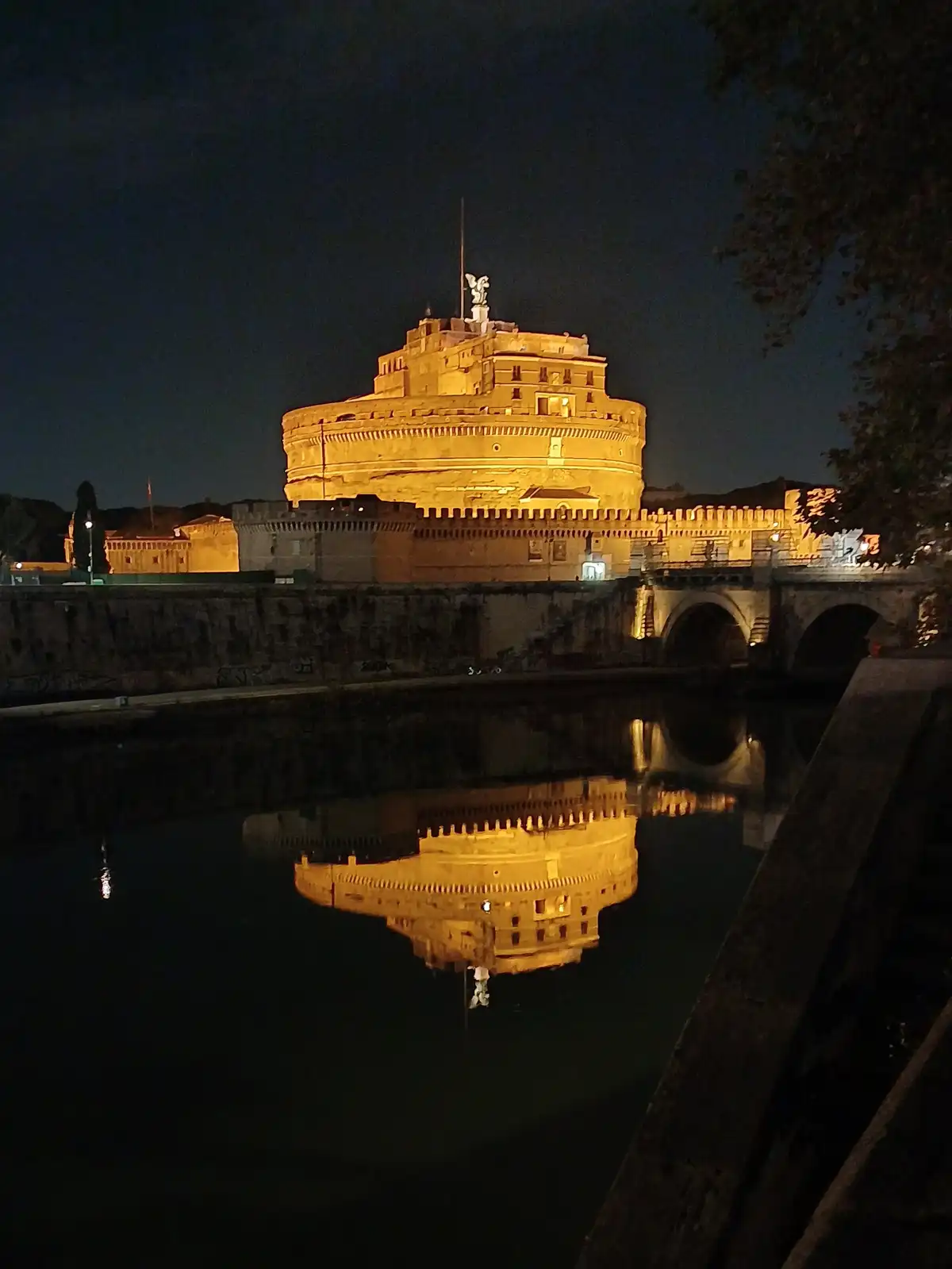 A nighttime photograph shows the Castel Sant'Angelo in Rome, its stone structure brightly illuminated against a dark sky…