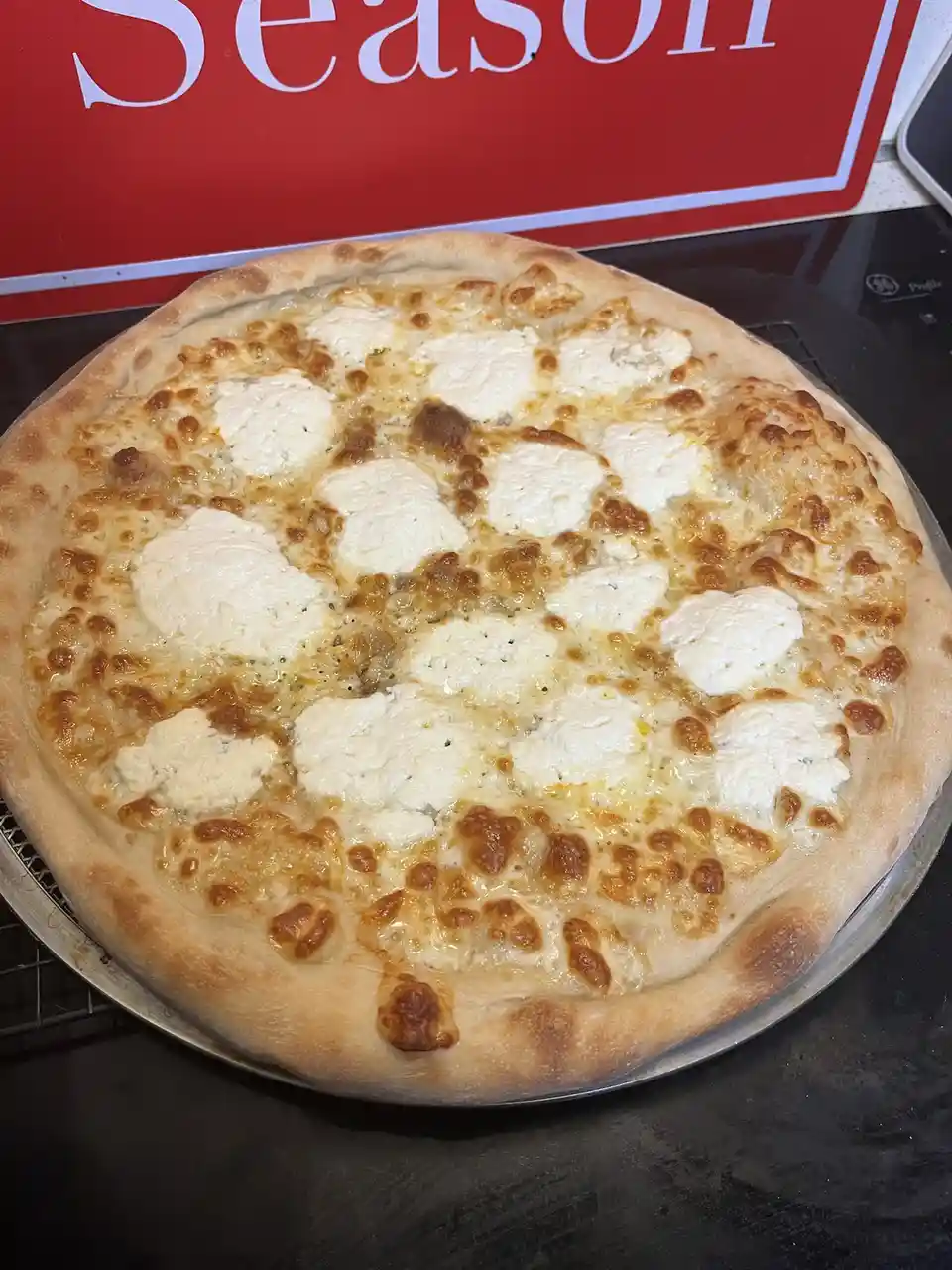 A freshly baked pizza with golden-brown crust and melted cheese topped with dollops of white cheese sits on a metal tray…