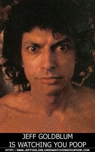 A grainy, close-up photo of actor Jeff Goldblum with a serious, intense stare, shirtless and with dark curly hair. The image…