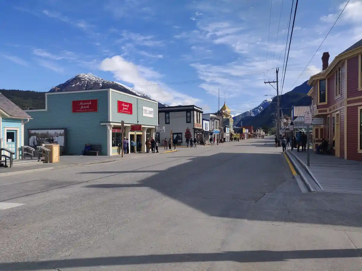 A wide street in a small town with colorful storefronts like 'Monarch Jewels' and 'THE LOOM', set against snow-capped…