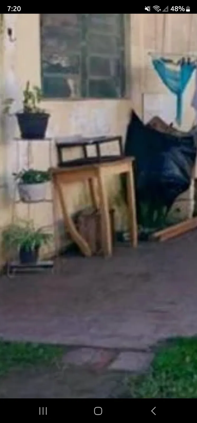 A blurry photo of a cluttered outdoor patio area with a wooden chair leaning against a small table, potted plants on a…