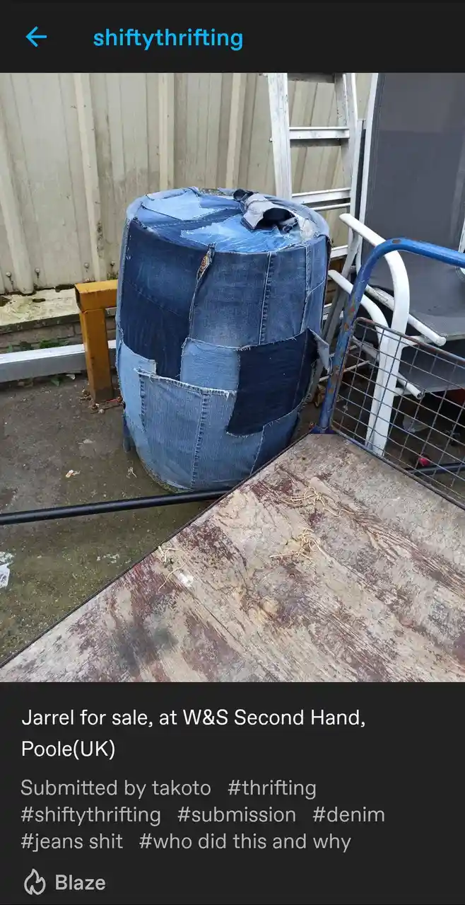 A large, cylindrical barrel is covered in mismatched, frayed denim patches, including a pocket, and sits outdoors next to a…