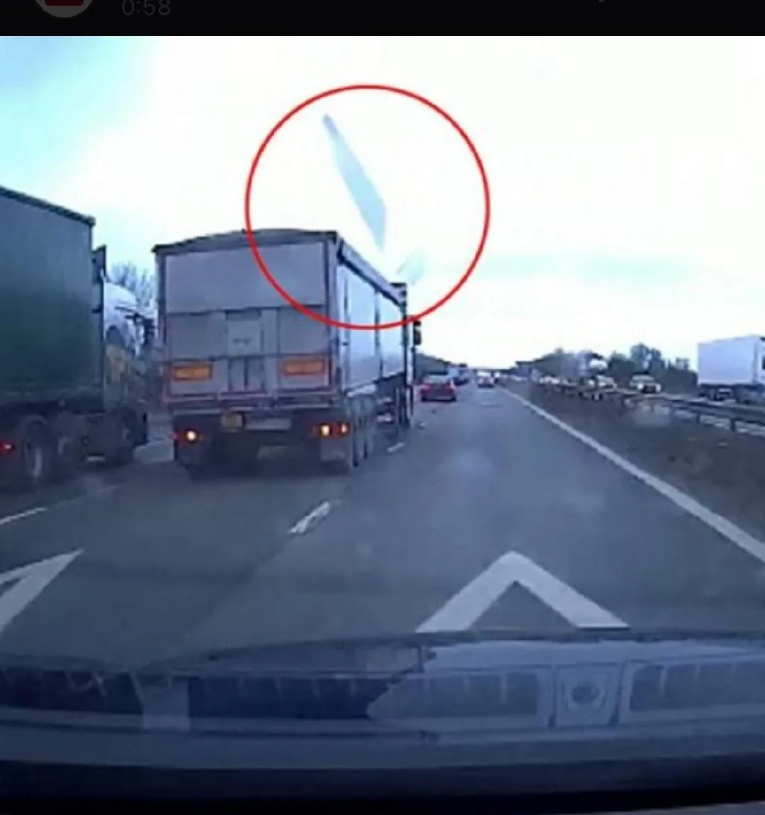 A dashcam view from a car on a multi-lane highway shows a large white semi-truck ahead, with a red circle drawn around a…
