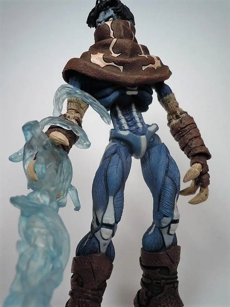A blue-skinned action figure with muscular definition, wearing brown armor and wielding a translucent blue weapon, stands…