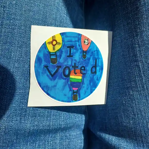 A circular sticker with the text 'I voted' is stuck on a blue denim jacket. The sticker features a blue sky background with…