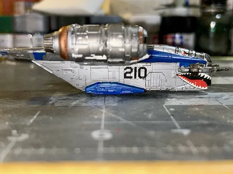 A detailed scale model of a futuristic spaceship, painted silver and blue with the number '210' on its side and a…
