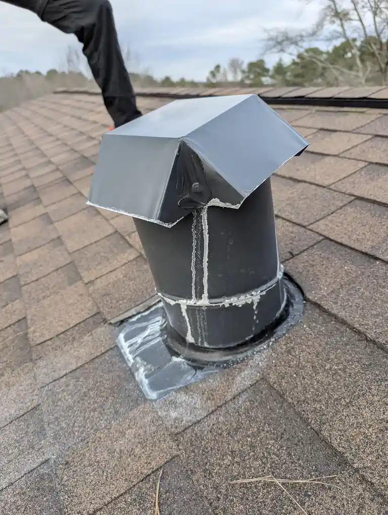 A close-up photo shows a black roof vent on a shingled roof with visible white caulk or sealant dripping down its sides and…