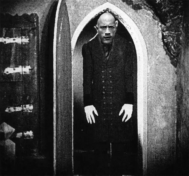 A black-and-white image shows a bald man in a dark, buttoned coat standing in a gothic archway, looking shocked with his…