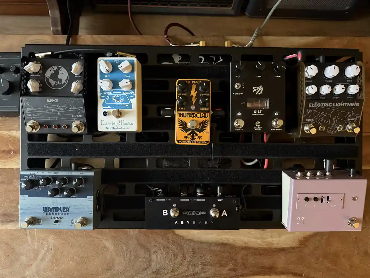 An overhead shot of a black pedalboard holding multiple guitar effects pedals, including a blue 'Dispatch Master' pedal with…