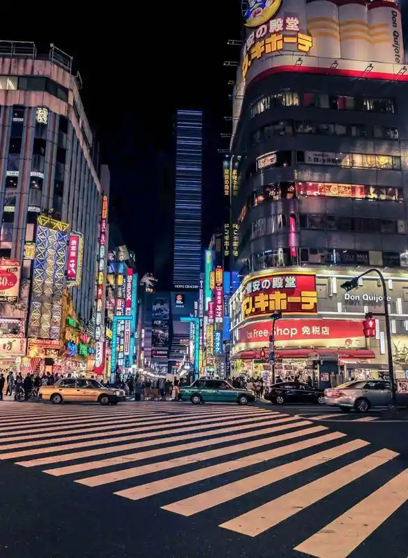 A vibrant nighttime photograph of a bustling Tokyo street, likely Shibuya, filled with towering buildings adorned with…