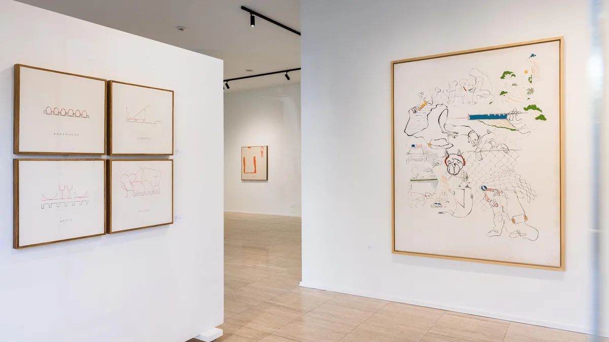 An art gallery interior with white walls and light wood floors, displaying minimalist framed artworks on the left and a…