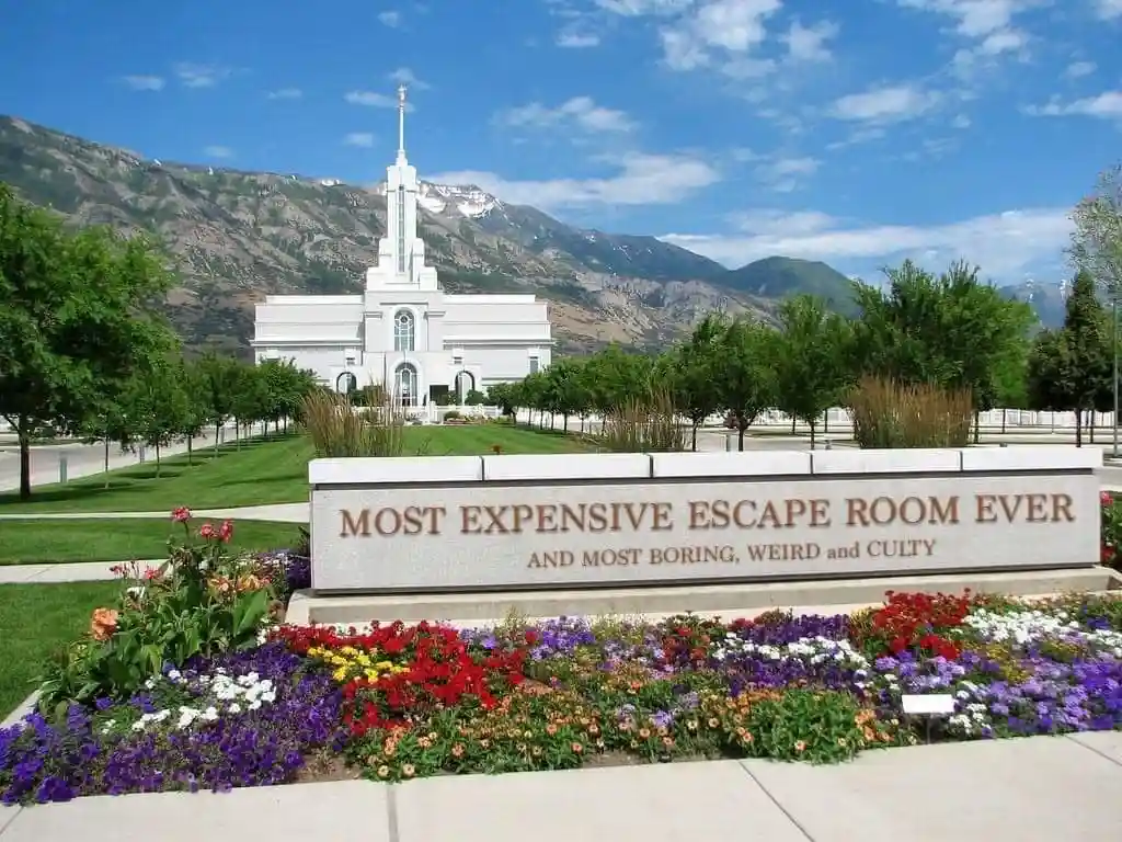 A large stone sign in front of a white temple with mountains in the background reads 'MOST EXPENSIVE ESCAPE ROOM EVER AND…