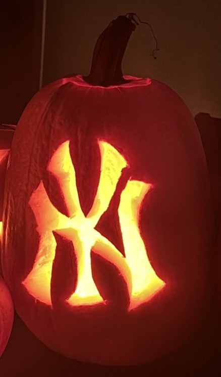 A close-up of a carved pumpkin illuminated from within, featuring the iconic interlocking 'NY' logo of the New York Yankees…