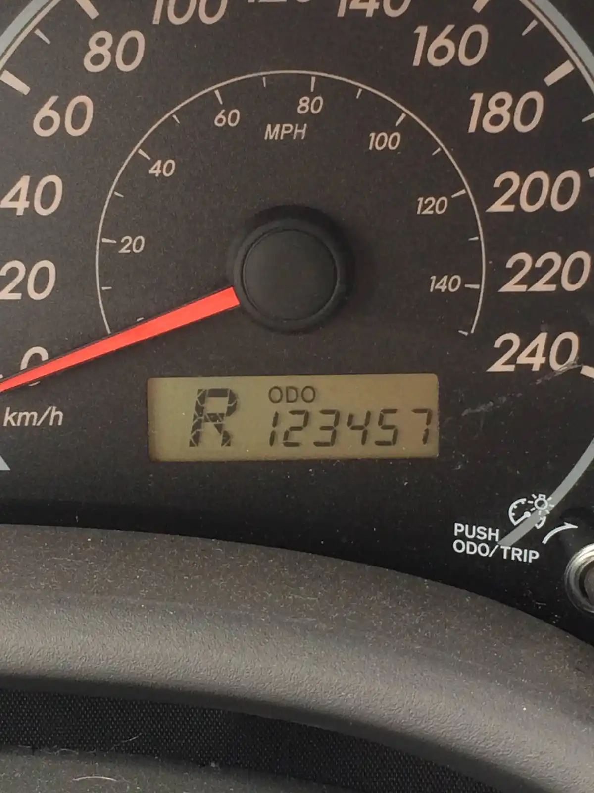 A close-up of a car's dashboard showing a speedometer with MPH and km/h markings, the needle at zero, and a digital odometer…