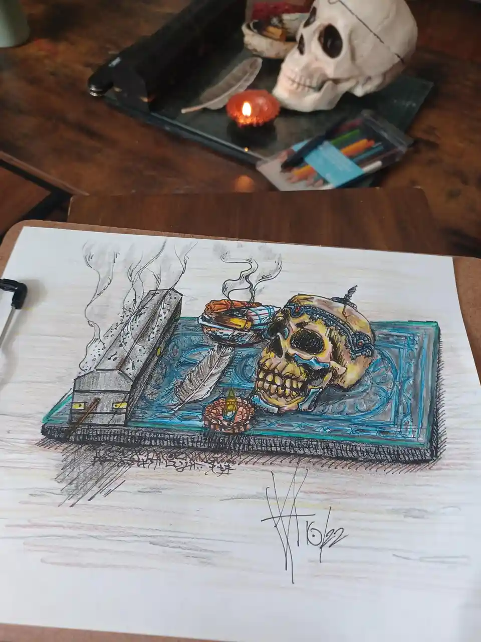 A hand-drawn illustration on paper depicts a skull resting on a phone, surrounded by mystical items like incense, feathers…