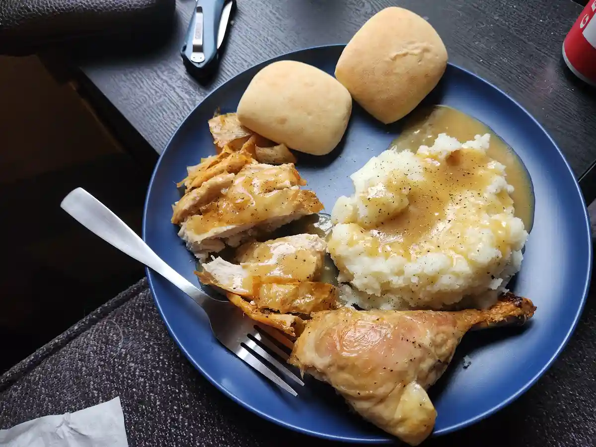 A blue plate holds a home-cooked meal featuring sliced roasted chicken, mashed potatoes topped with gravy, and two dinner…