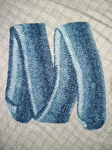 Two hand-knitted socks in a blue and white gradient pattern lie side by side on a grey and white floral-patterned fabric…
