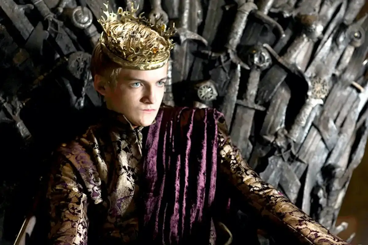 a young man with blonde hair and blue eyes wears a golden crown and sits on a throne made of swords, dressed in a purple and…