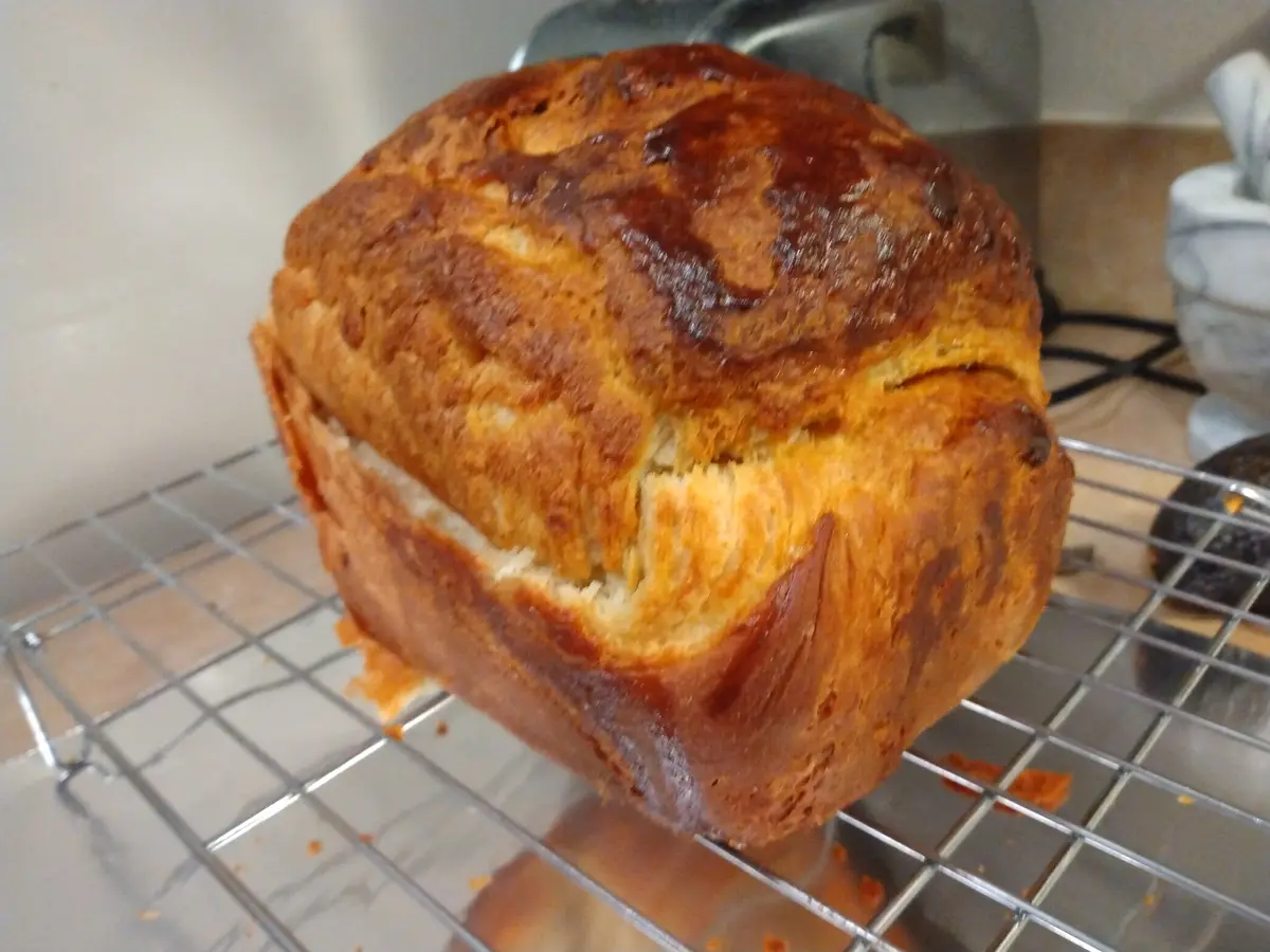 A freshly baked loaf of bread with a golden-brown crust sits on a metal cooling rack, its top and side showing a distinct…
