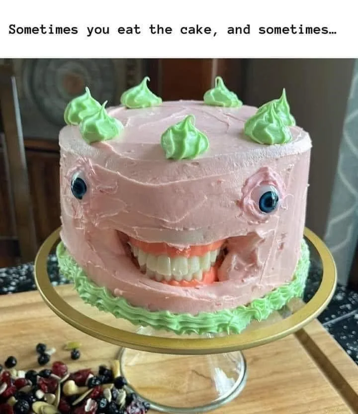 A round pink-frosted cake decorated with green frosting dollops on top and a cartoonish face made of frosting, featuring…