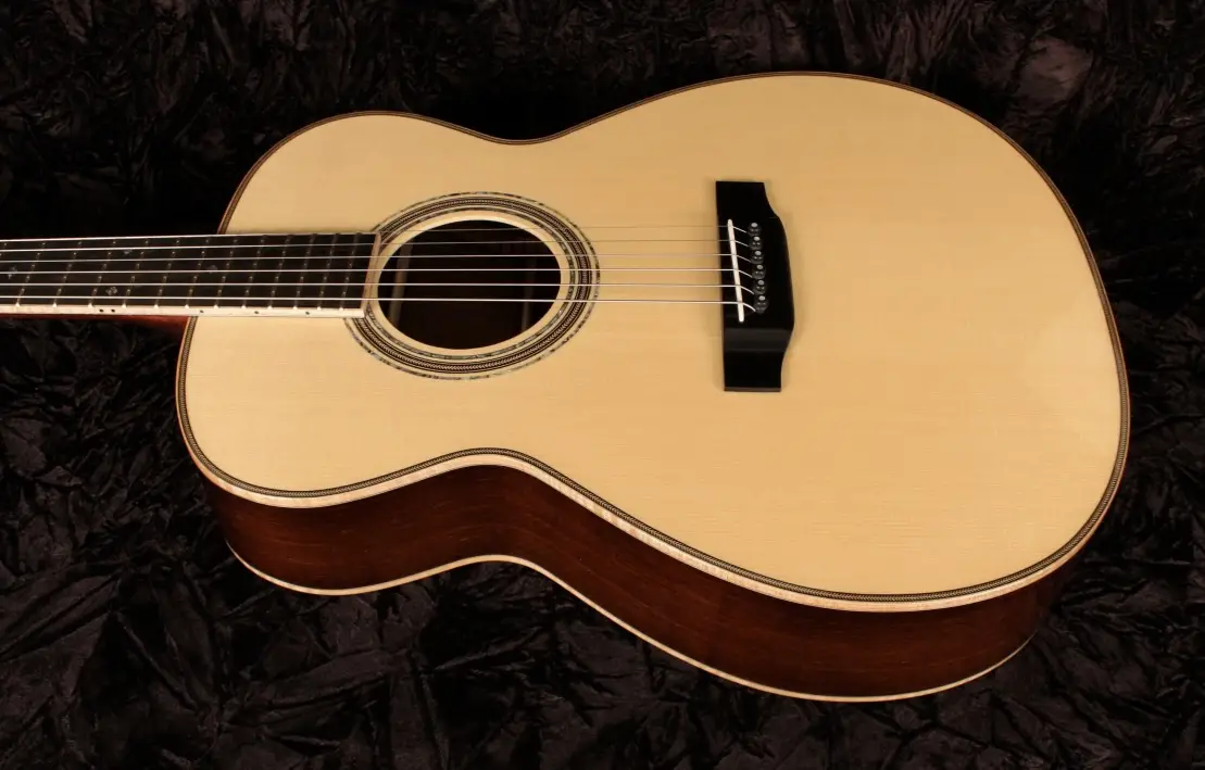 A close-up photo of a light-wood acoustic guitar with a dark fretboard and black bridge, resting on a crumpled black fabric…