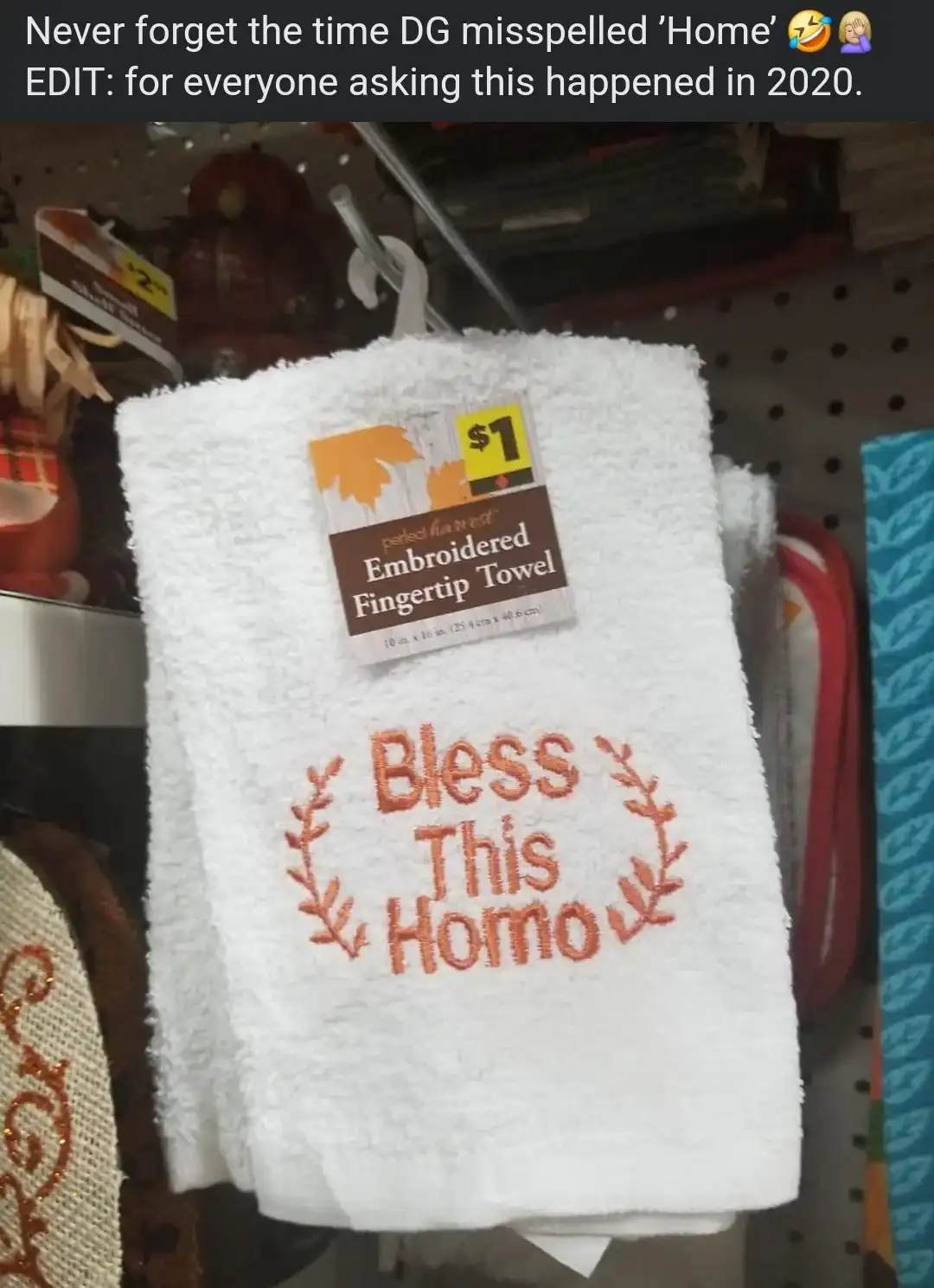 A white embroidered fingertip towel hangs on a store shelf, priced at $1. The towel features the phrase 'Bless This Homo'…