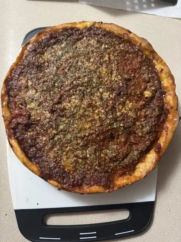A freshly baked pizza with a thick crust, red sauce, and a generous topping of herbs and cheese sits on a white and black…