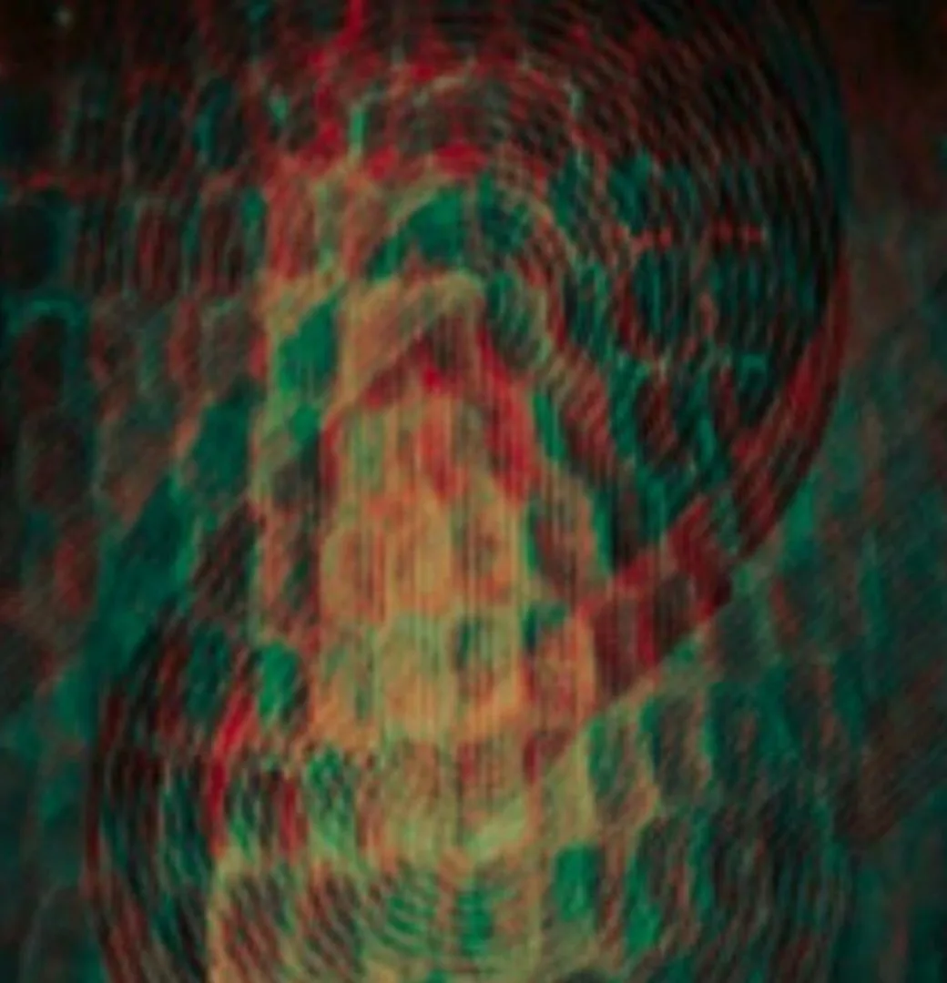 A heavily distorted, glitchy, and abstract image with swirling red, green, and black patterns that vaguely resemble a face…