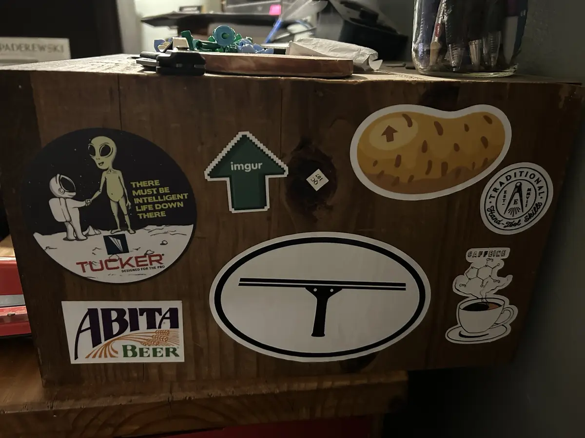 A wooden box covered in various stickers including an alien handshake with the text 'there must be intelligent life down…