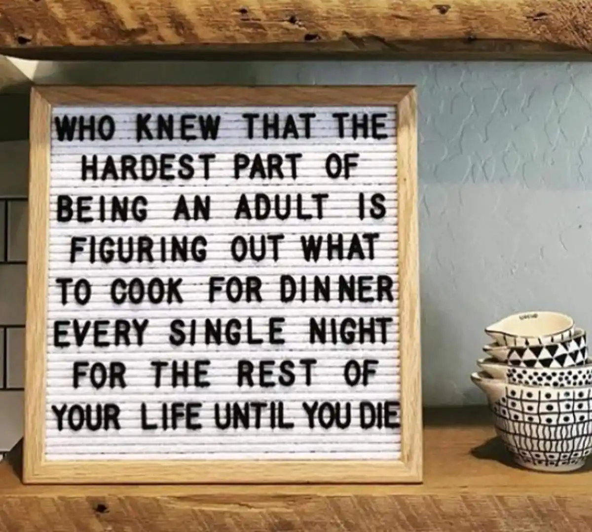A wooden-framed letterboard sits on a rustic wooden shelf, displaying the text 'WHO KNEW THAT THE HARDEST PART OF BEING AN…