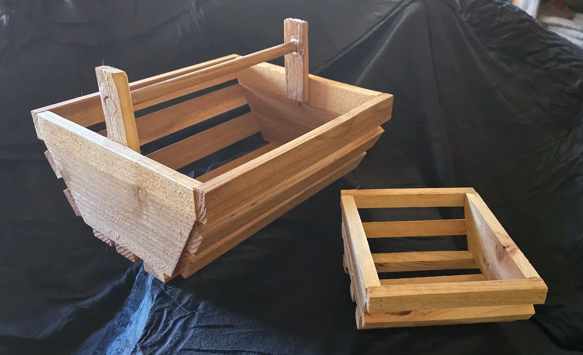 Two wooden crates are shown on a black fabric surface; one is assembled into a boat shape with a handle, the other is a…